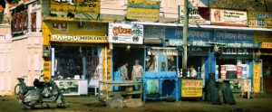 Two men talking in doorway of shop, in a row of colourful shops, India